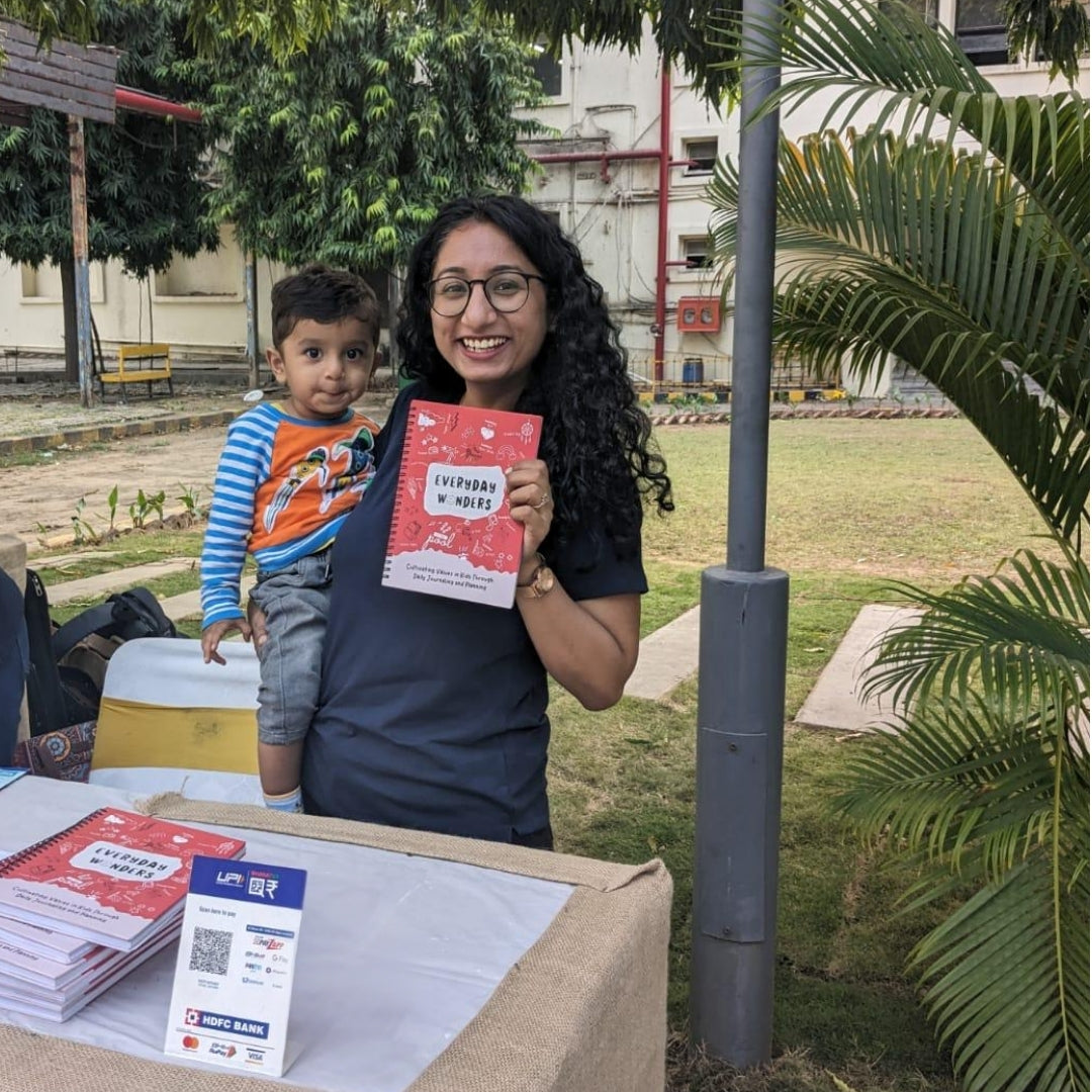 Founder of The Wonder Whale holding the Everyday Wonders kids journal with a toddler at a family-friendly outdoor event promoting growth and journaling for children.