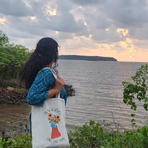 Person standing by the seaside at sunset carrying The Wonder Whale Bringing Big Dreams canvas tote bag while enjoying a peaceful travel moment in nature.