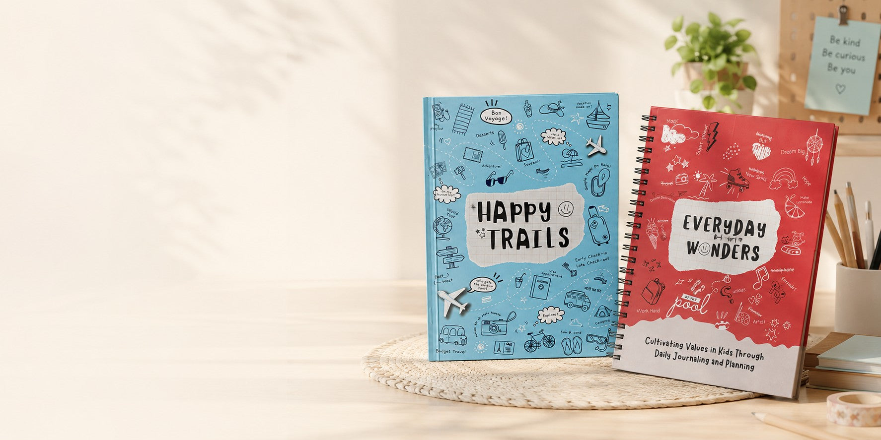 Two notebooks, one blue and one red, with 'Happy Trails' and 'Everyday Wonders' text on a light background.